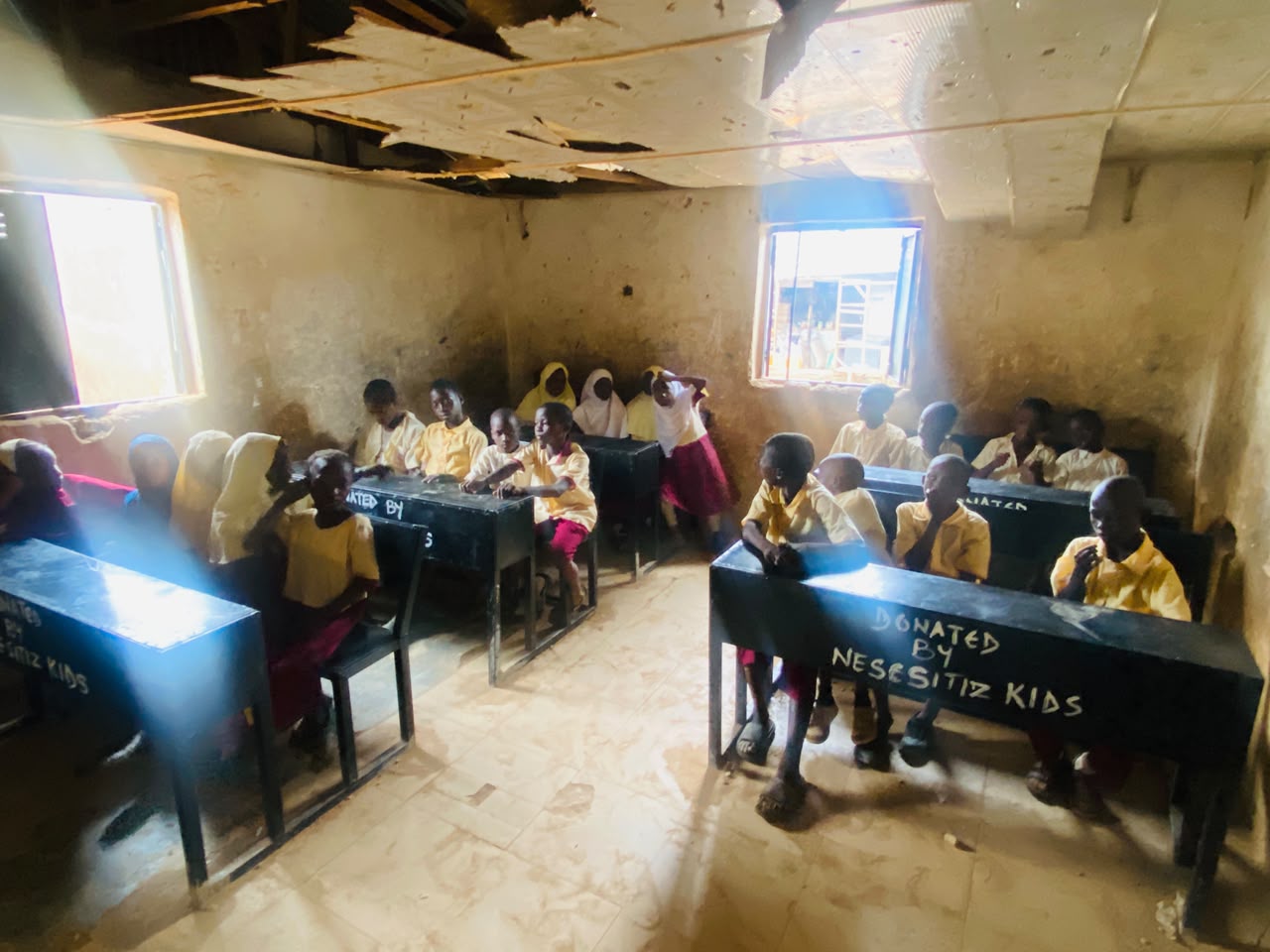 Children seated at desks donated by Nesesitiz Kids